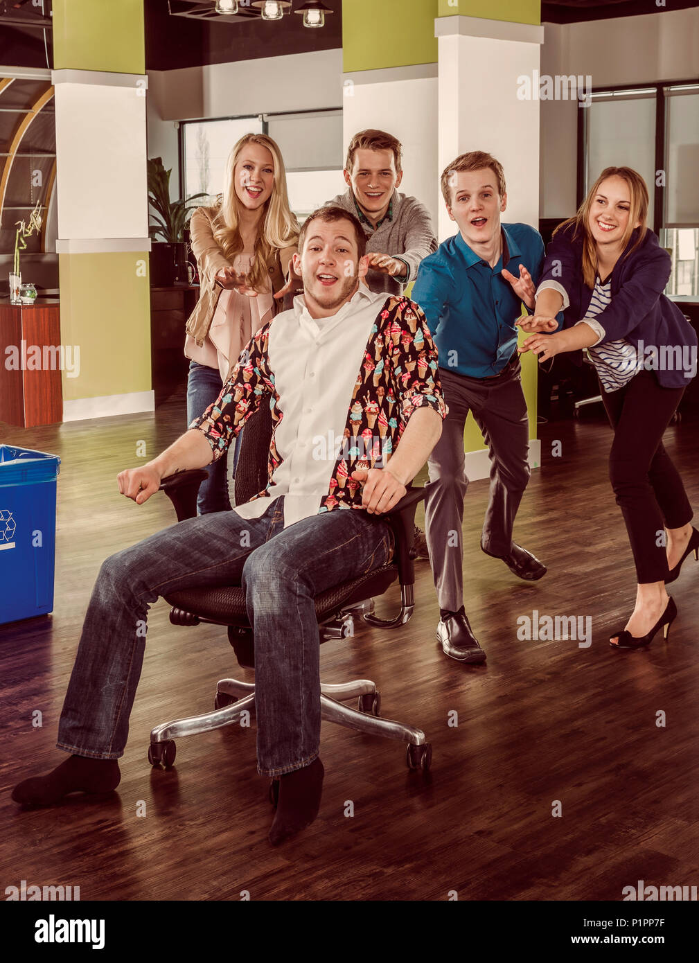 Gruppe Junger millennials Drücken ein Mitarbeiter über den Raum in seinem Stuhl; Sherwood Park, Alberta, Kanada Stockfoto