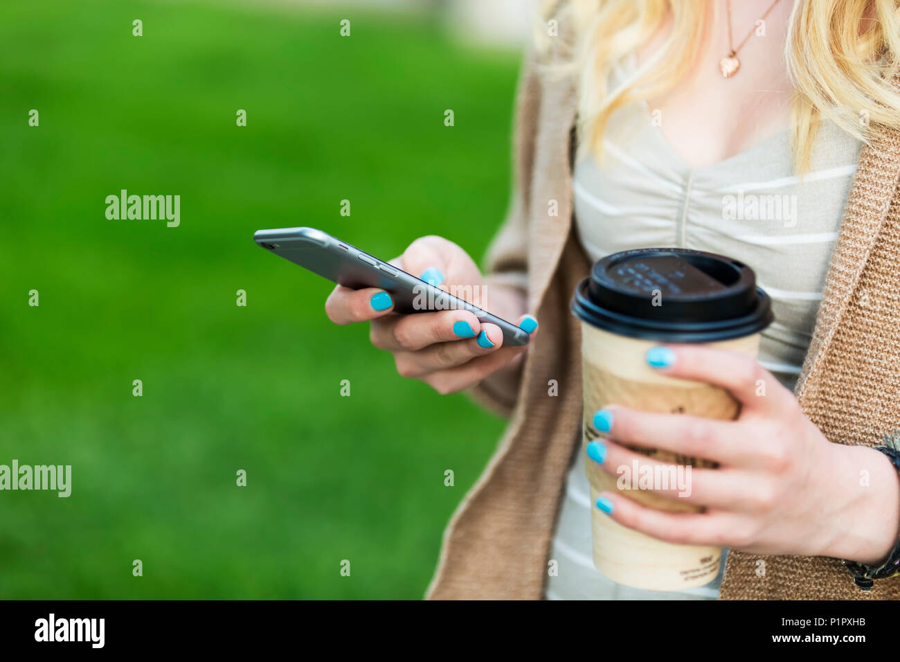 Nahaufnahmen der Hände ist eine junge Frau mit blauen Nagellack Holding eine Tasse Kaffee und Textnachrichten auf Ihrem smart phone; Edmonton, Alberta, Kanada Stockfoto