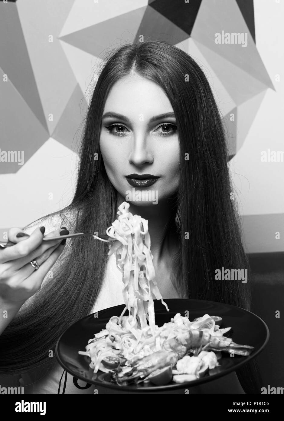 Portrait von attraktiven Langhaarige Frau mit etwas angelehnt Mund und rote Lippen essen Italienische Pasta mit Meeresfrüchten und Gemüse. Wunderschöne junge Frau Stockfoto