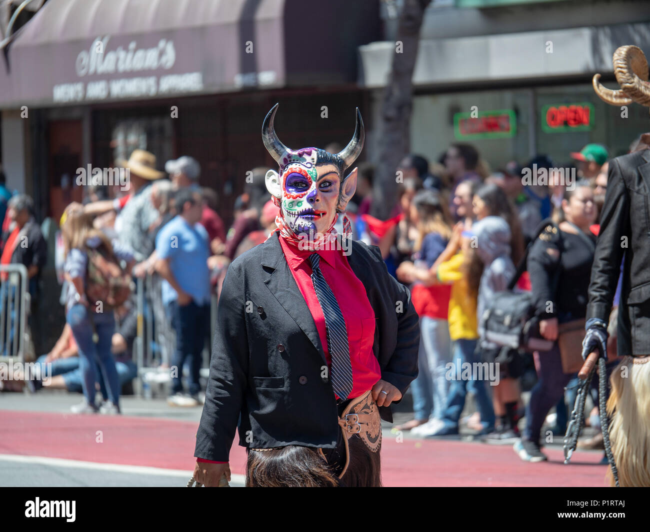 Eine Frau trägt ein Teufel Maske und Rissbildung eine Peitsche geht hinunter die Straße an einer Parade Stockfoto