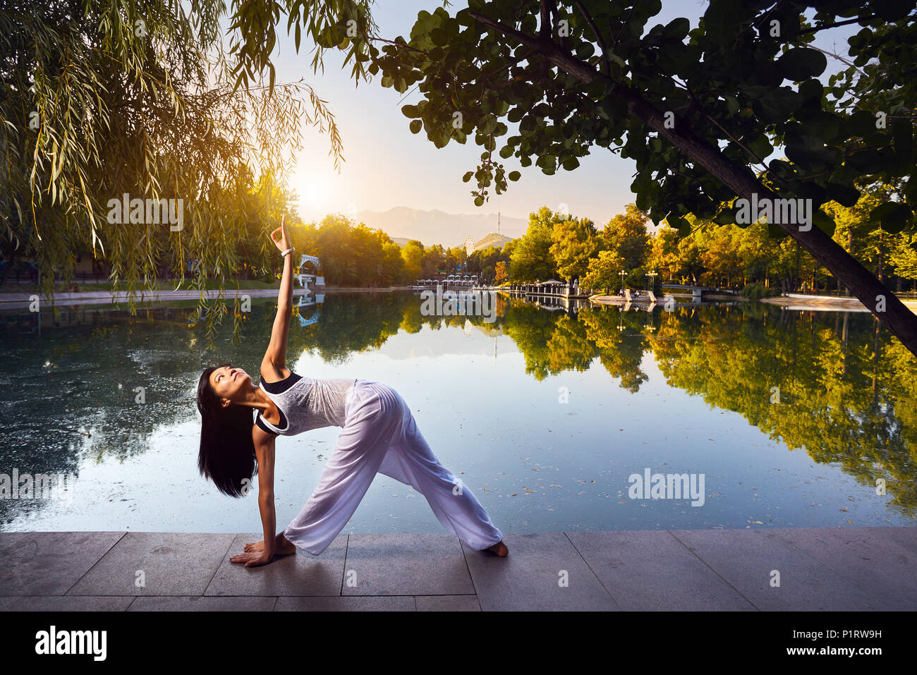 Schöne asiatische Mädchen im weißen Kostüm Yoga in der Nähe der See im Park bei Sonnenaufgang Stockfoto