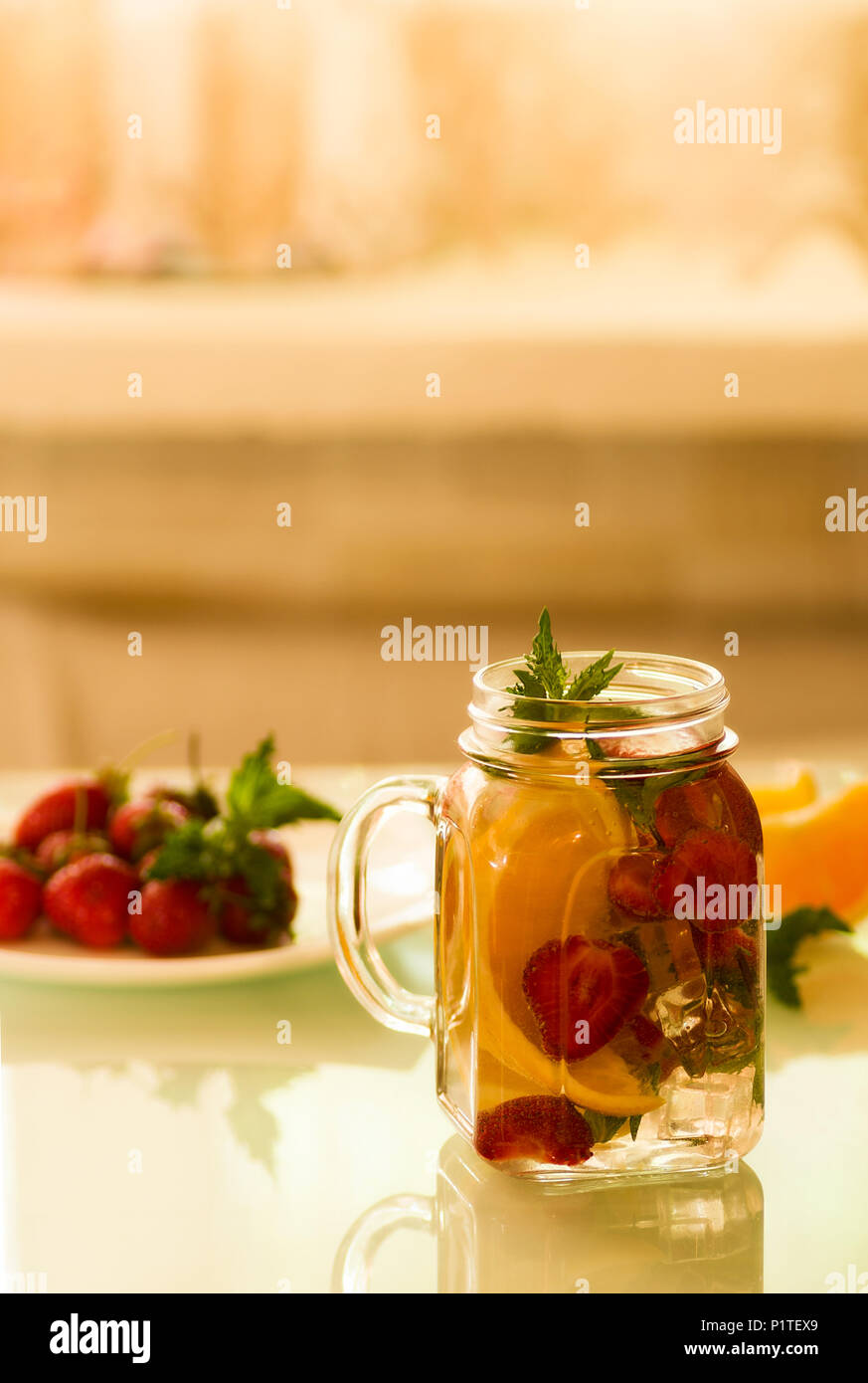 Stillleben mit einer Flasche in Scheiben geschnittene Orangen und Erdbeeren auf einem weißen Tisch, bio-veganen Milch Stockfoto