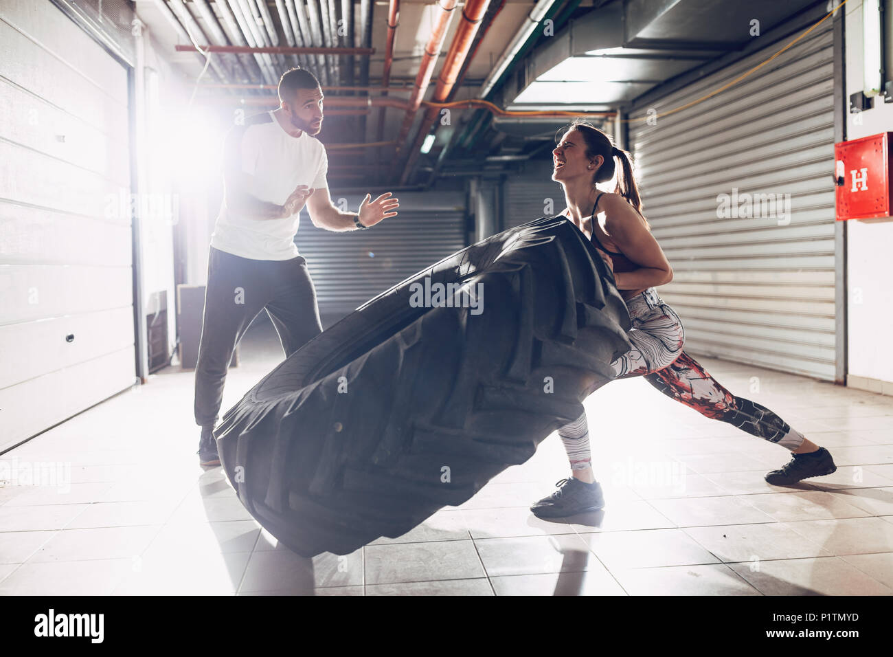 Junge muskulöse Frau spiegeln ein Reifen auf hartes Training mit Personal Trainer an der Garage Gym. Stockfoto