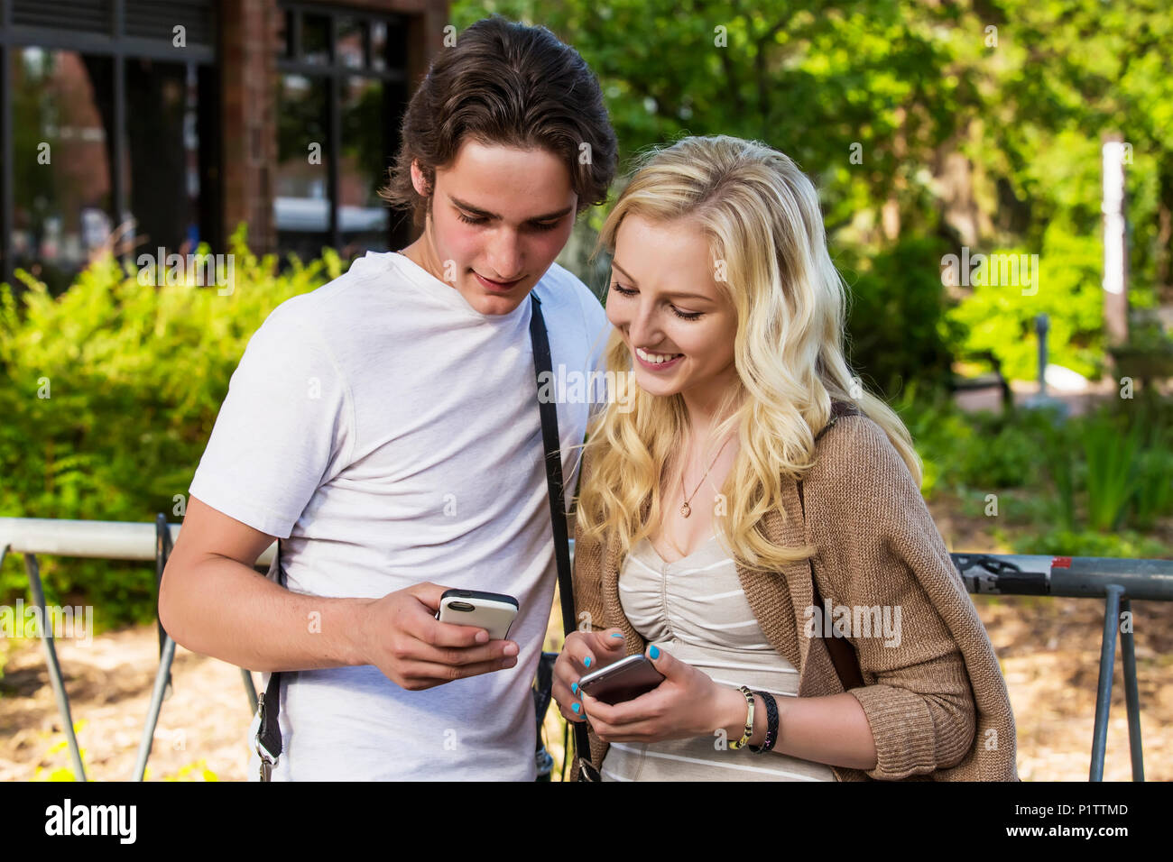 Ein junges Paar steht auf dem Campus der Universität an Ihren smart phones zu zeigen jede andere soziale Medien Beiträge; Edmonton, Alberta, Kanada Stockfoto