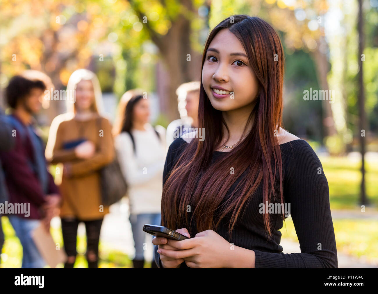 Portrait einer jungen Frau an der Internationalen Universität student Holding ein smart phone mit Ihren Freunden im Hintergrund stehend Stockfoto
