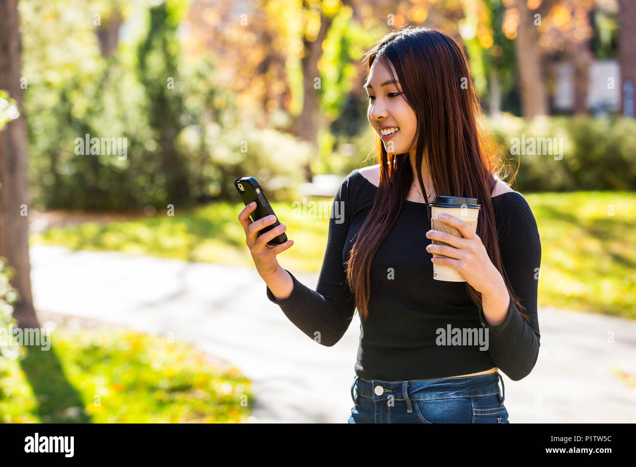 Ein junger Chinese International Student steht eine Kaffeetasse und mit Ihrem Smart Phone auf einem Campus der Universität; Edmonton, Alberta, Kanada Stockfoto