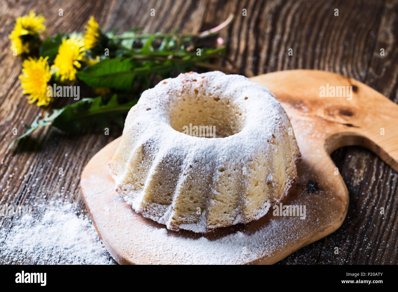 Hausgemachten Gugelhupf mit Puderzucker auf einem ländlichen Holzplatte auf dem Hintergrund der Frühling Löwenzahn Stockfoto