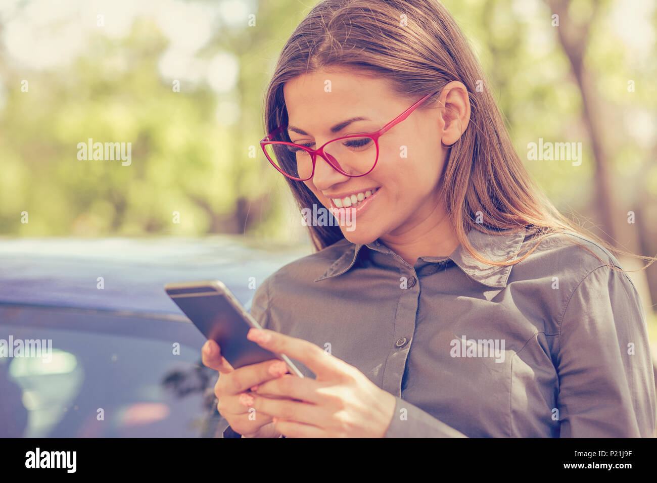 Junge Frau von SMS-Nachrichten auf dem Smartphone im Freien an einem sonnigen Tag im Herbst Stockfoto