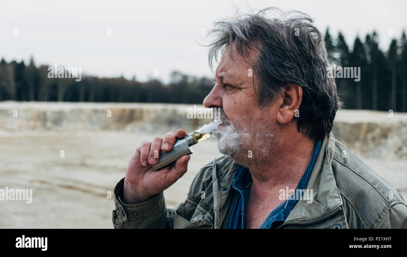 Alter Mann mit casual Outfit ist Rauchen E-Zigarette im Wald Stockfoto