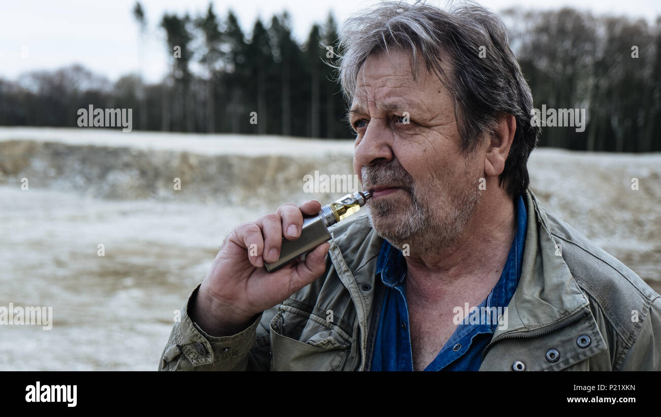 Alter Mann mit casual Outfit ist Rauchen E-Zigarette im Wald Stockfoto