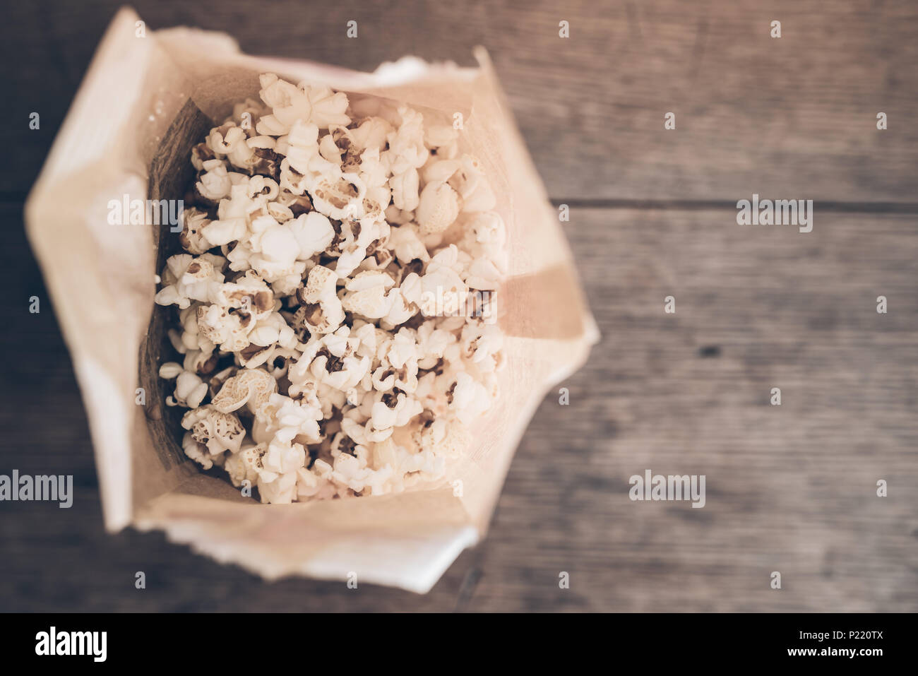 Ansicht von oben frisches Popcorn in der braunen Papiertüte auf rustikalen Holztisch Stockfoto