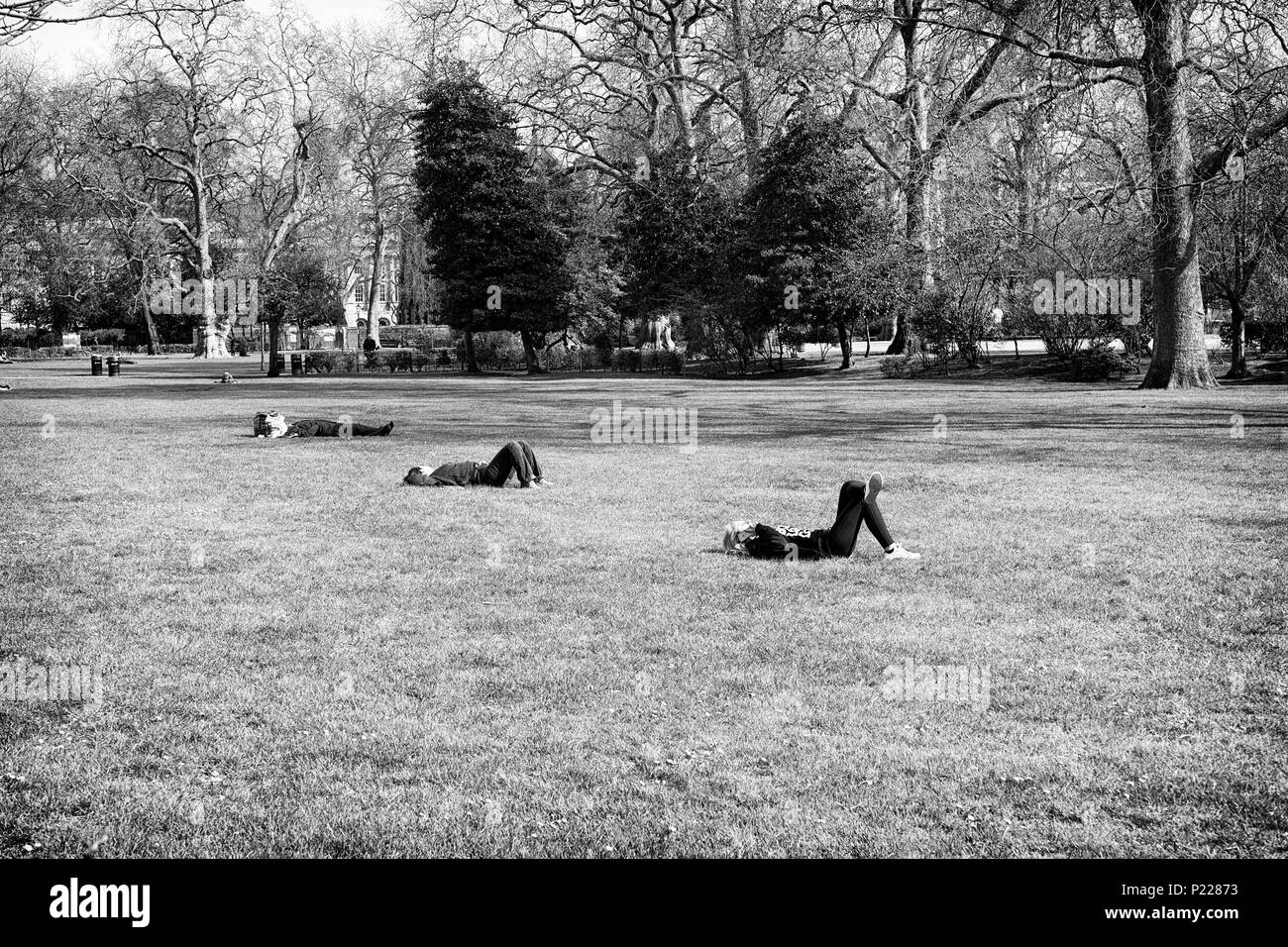 Drei Leute liegen mit ihren Knien in einem Park in London. Stockfoto