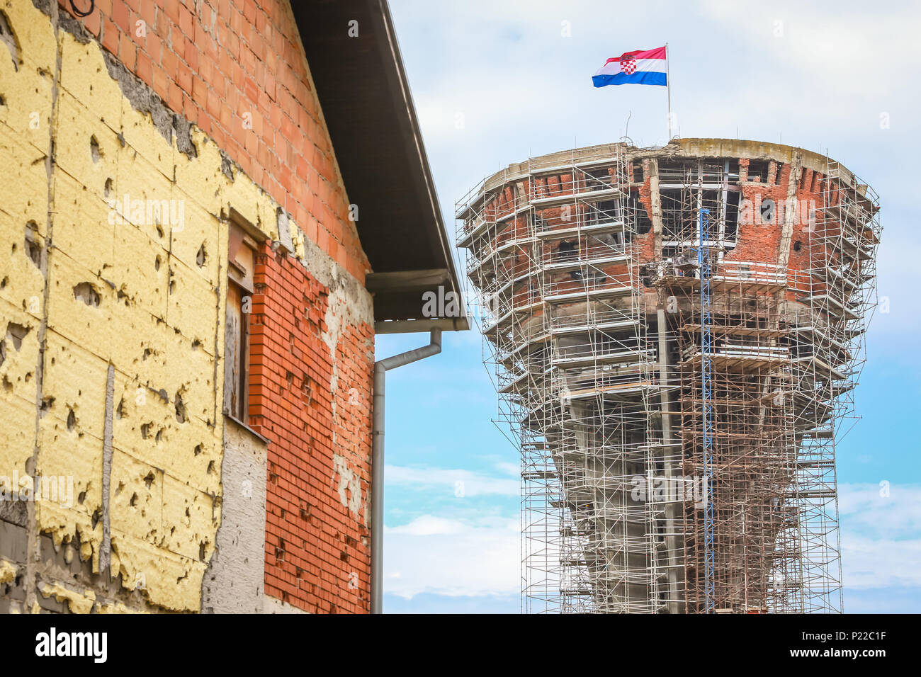 Ein Blick auf die vukovar Wasserturm unter Rekonstruktion mit einem Haus in Krieg in Vukovar, Kroatien beschädigt. Der Wasserturm ist ein Wahrzeichen der Stadt Leiden Stockfoto