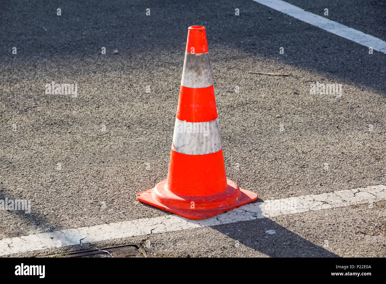 Leitkegel, mit weißen und orangefarbenen Streifen auf grauem Asphalt, Stockfoto