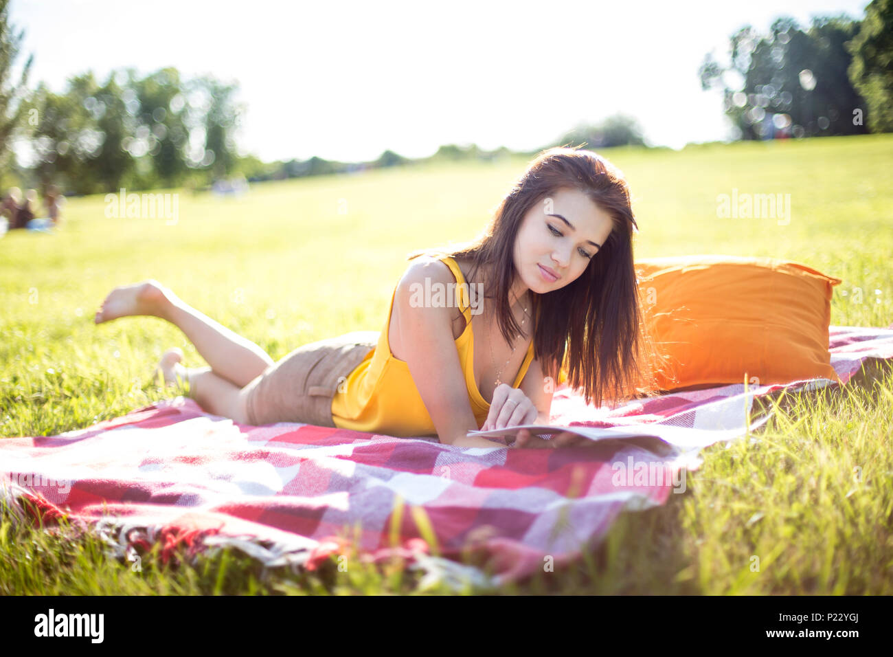 Junge attraktive Frau liest eine Zeitschrift auf einer Wiese in einem Park Stockfoto