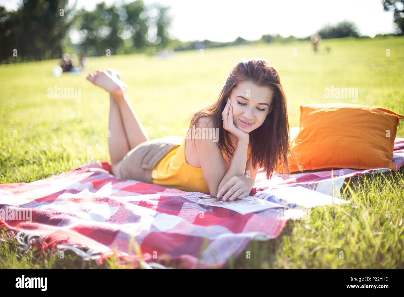 Junge attraktive Frau liest eine Zeitschrift auf einer Wiese in einem Park Stockfoto