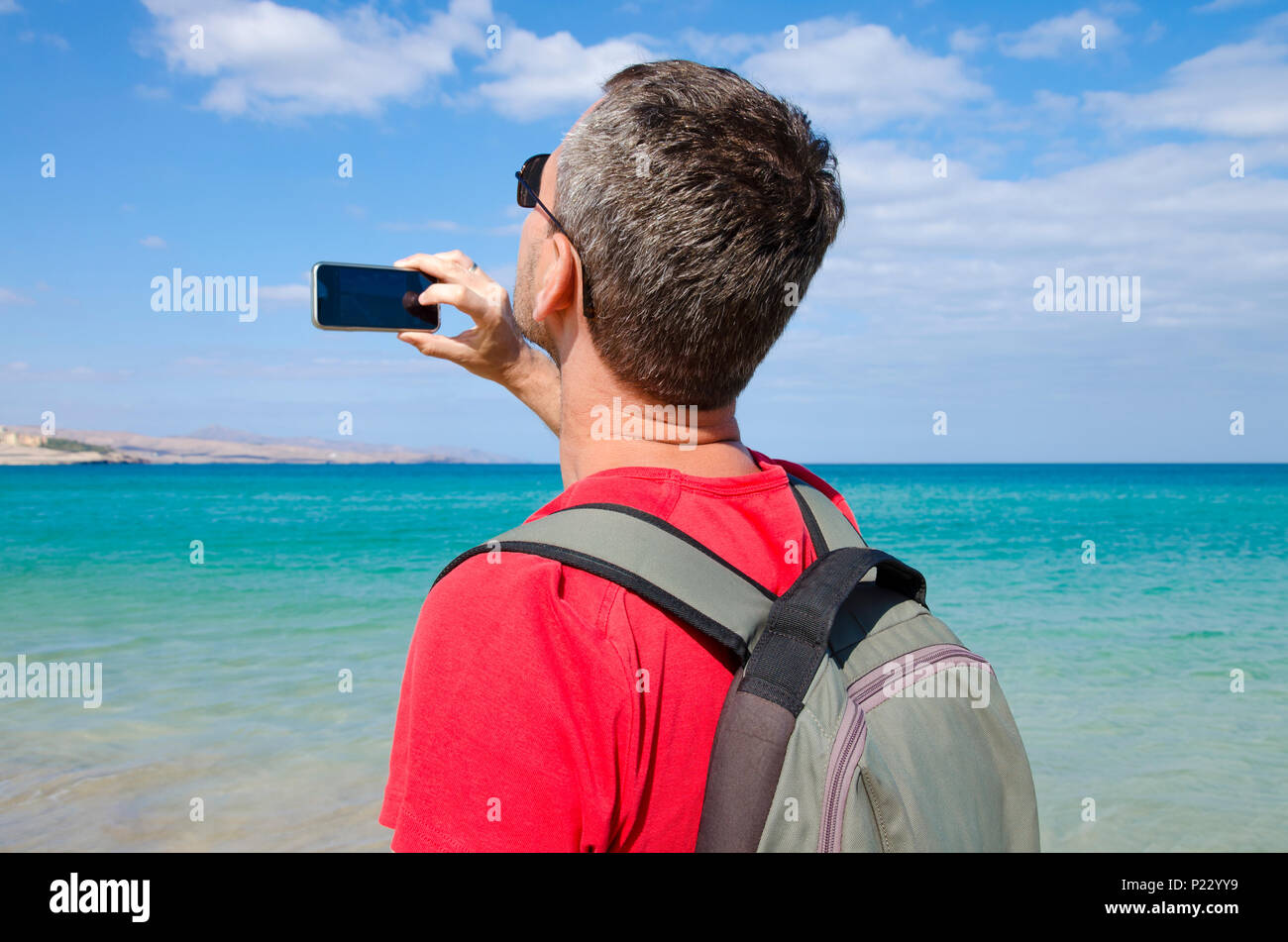 Ein Tourist am Strand nimmt ein Foto auf das türkisfarbene Wasser und die Küste mit seinem Handy Stockfoto
