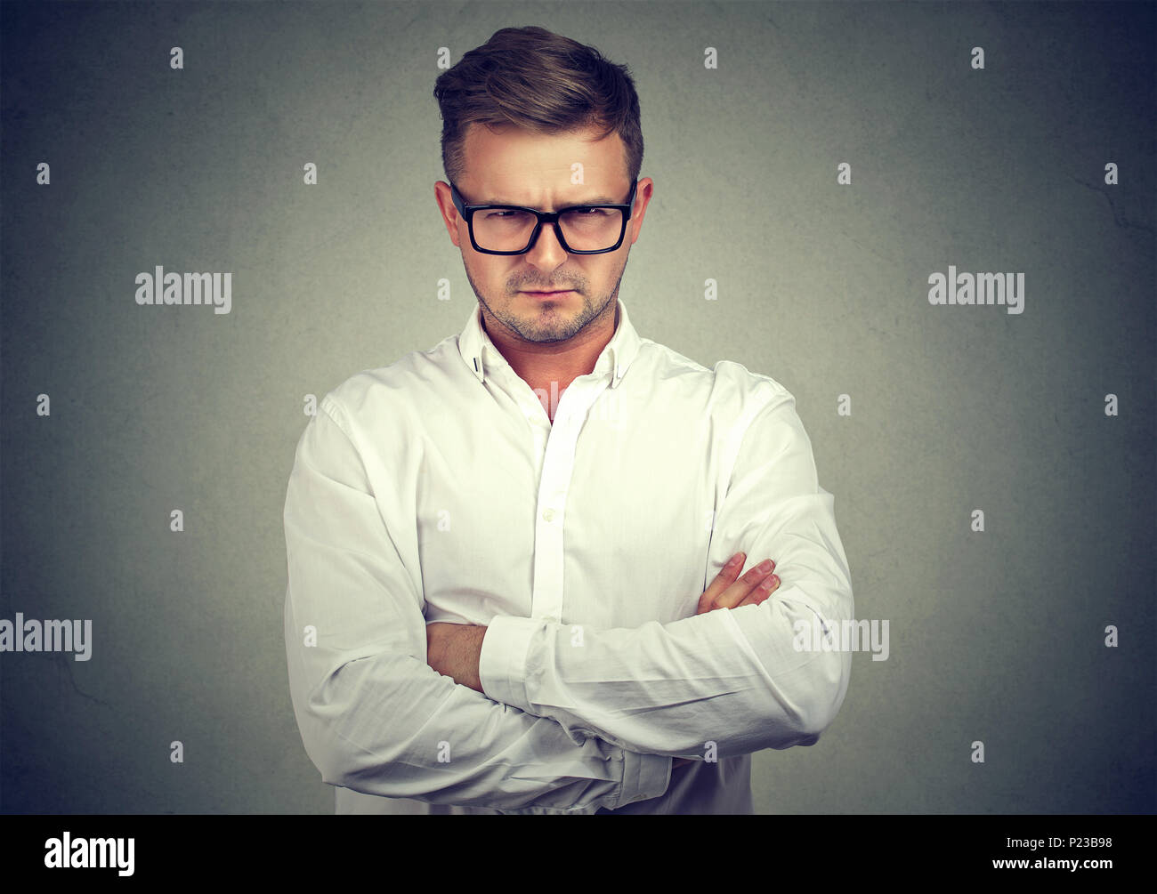 Ernster junger Mann in Gläser, Hände halten gekreuzt und Kamera in Abneigung auf grauem Hintergrund. Stockfoto