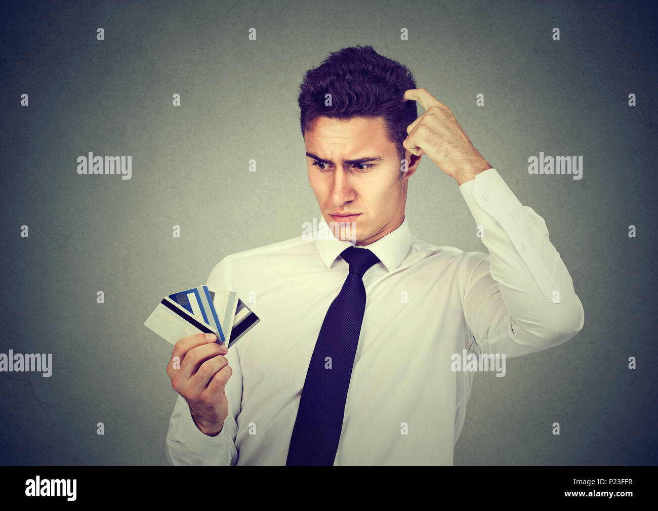 Verwirrt Mann an viele Kreditkarten unsicher welches auf grauem Hintergrund zu wählen Suchen Stockfoto