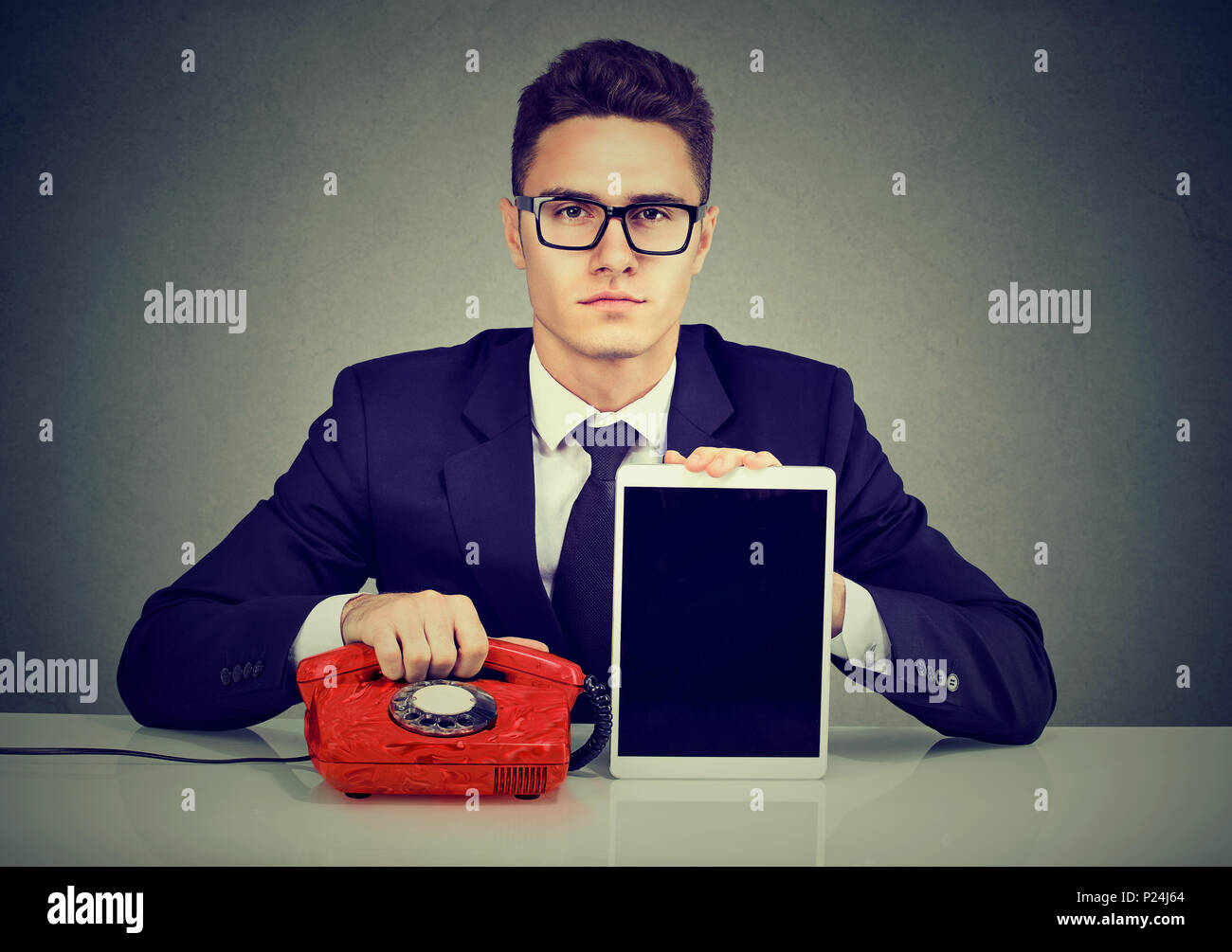 Ernsthafte Geschäftsmann am Schreibtisch sitzen und das altmodische Telefon und modernen Tablet Computer Stockfoto