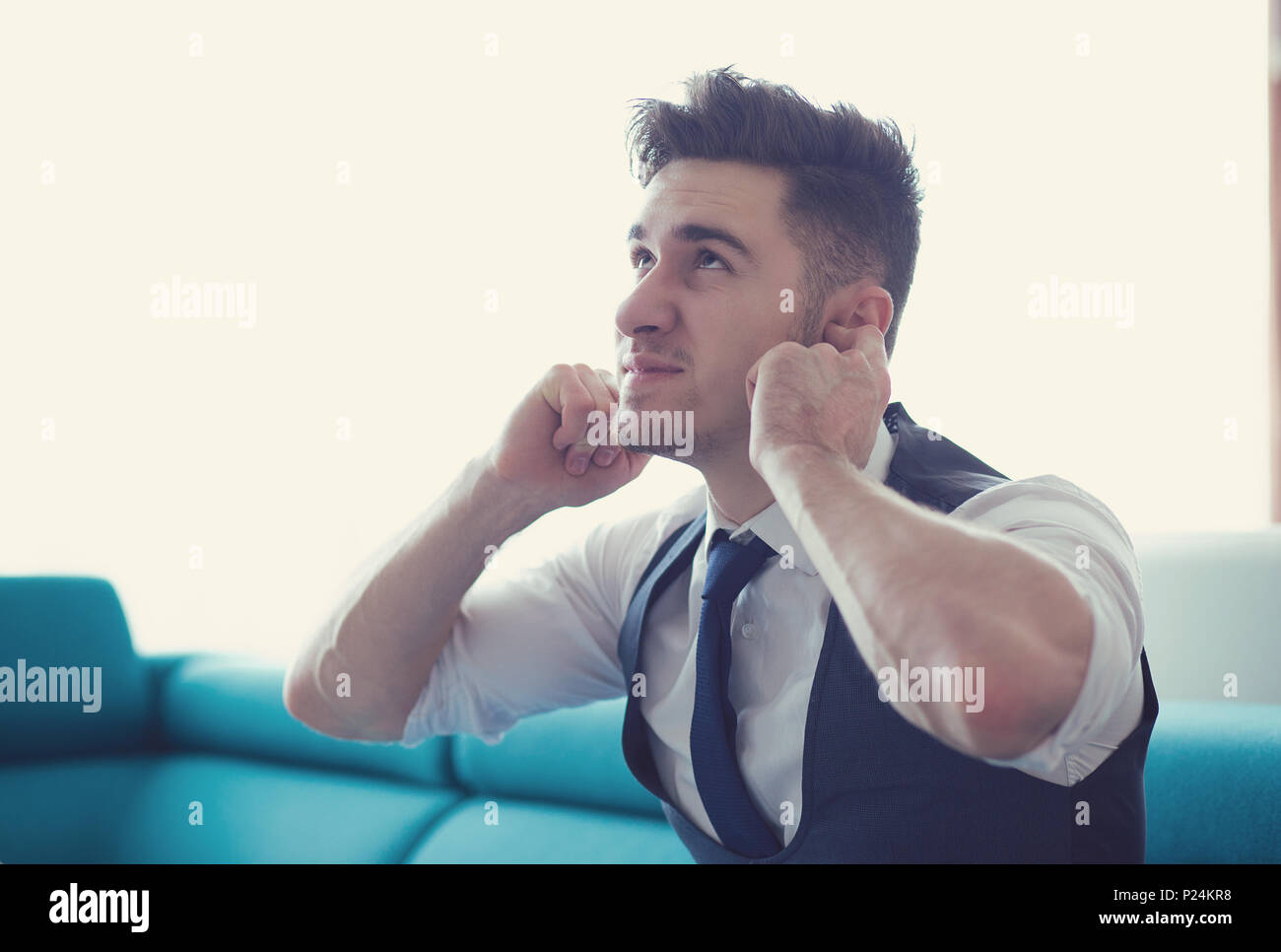 Junger Mann sitzt zu Hause auf der Couch, die Ohren mit lauten Nachbarn frustriert. Stockfoto