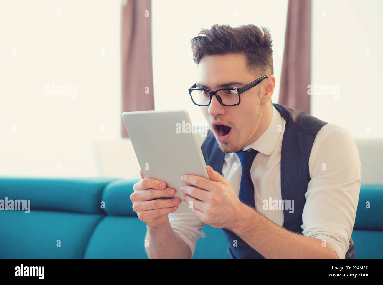 Jungen gutaussehenden Mann im tiefen Schock beobachten Tablet mit Rabatt aufgeregt. Stockfoto
