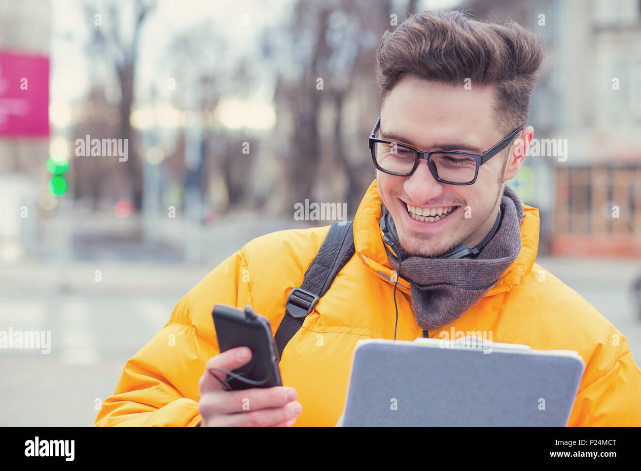 Inhalt happy männliche Kursteilnehmer in Brillen und Kopfhörer Messaging via Smartphone stehen auf der Straße. Stockfoto
