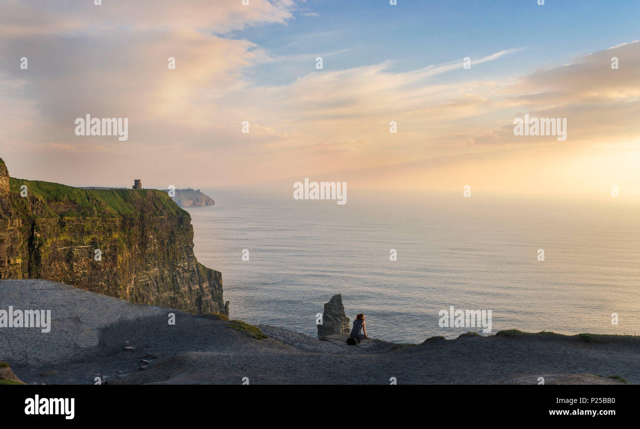 Die Klippen von Moher, Liscannor, Co. Clare, Provinz Munster, Irland. Eine Frau beobachten Sie den Sonnenuntergang auf einem Stein saß. Stockfoto