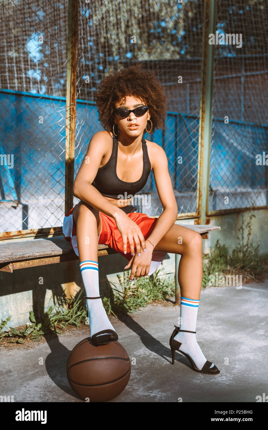 Junge afrikanische amerikanische Frau in sportliche Kleidung und High Heels  sitzt auf der Bank mit Basketball Ball unter Ihrem Fuß Stockfotografie -  Alamy