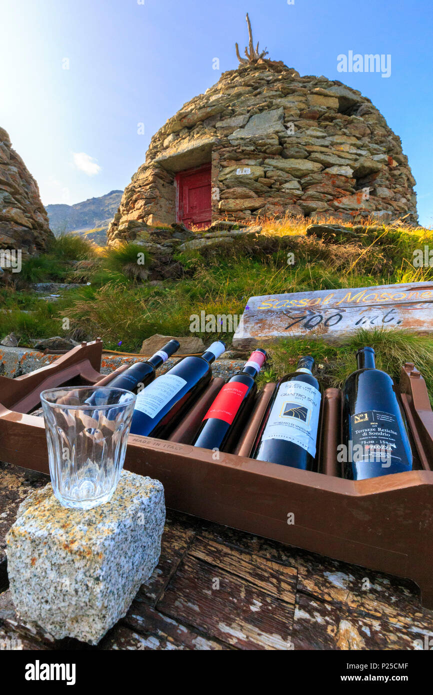 Wein und Glas mit traditionellen Keller im Hintergrund. Sassal Mason, Berninapass, Val Poschiavo, Graubünden, Schweiz. Stockfoto