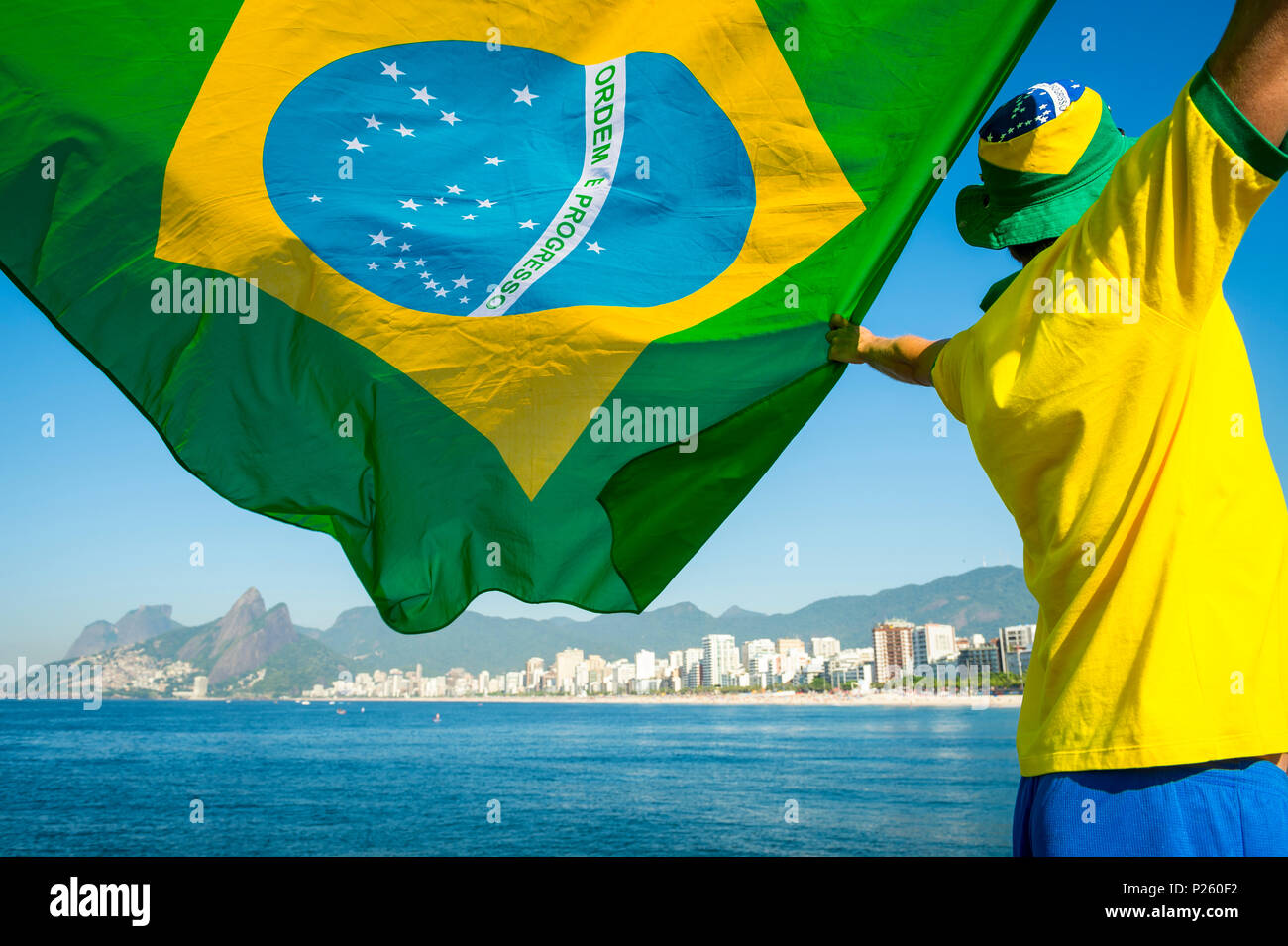 Brasilianischen Fußball-Fan flying Flagge vor der Strand von Ipanema Skyline der Stadt Rio de Janeiro. Stockfoto