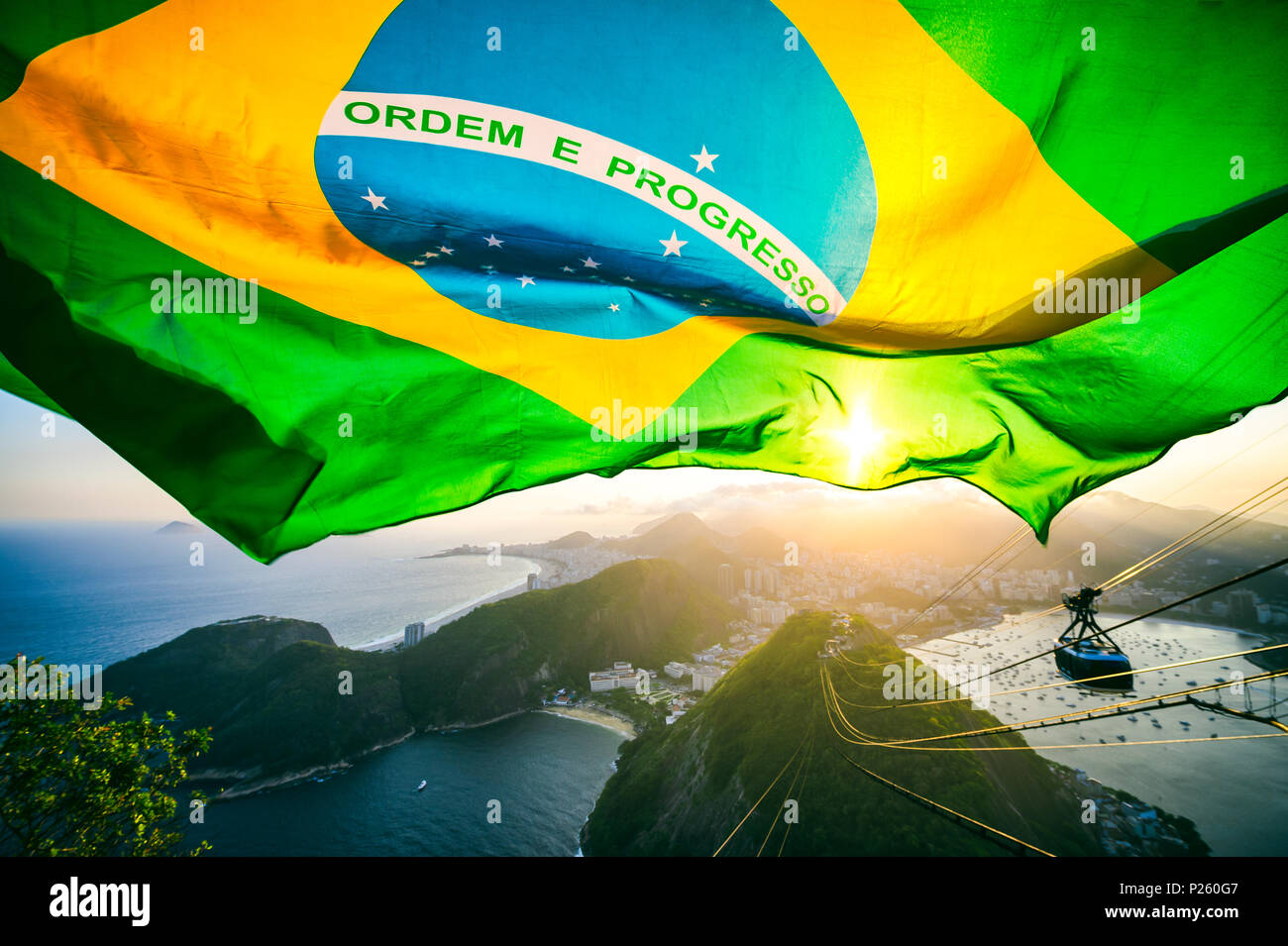 Brasilianische Flagge erstrahlt über dem goldenen Sonnenuntergang Skyline der Stadt am Zuckerhut in Rio de Janeiro. Stockfoto