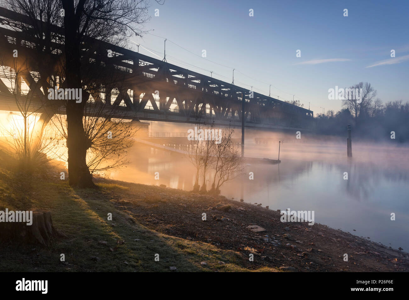 Strahlen von Licht durch die Ponte di Ferro in einer nebligen herbstlichen Morgen am Ufer des Flusses Ticino. Sesto Calende, Lago Maggiore, Provinz Varese, Lombardei, Italien. Stockfoto