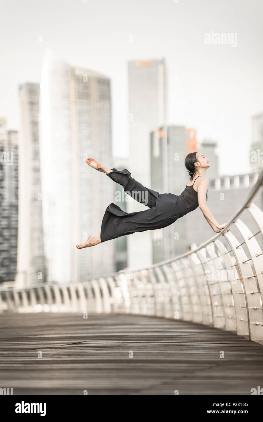 Nette junge Sportlerin führt eine perfekte straddle Sprung hoch, mit perfekter Kontrolle beim Lächeln, auf einer Brücke mit Hintergrund der Wolkenkratzer Stockfoto