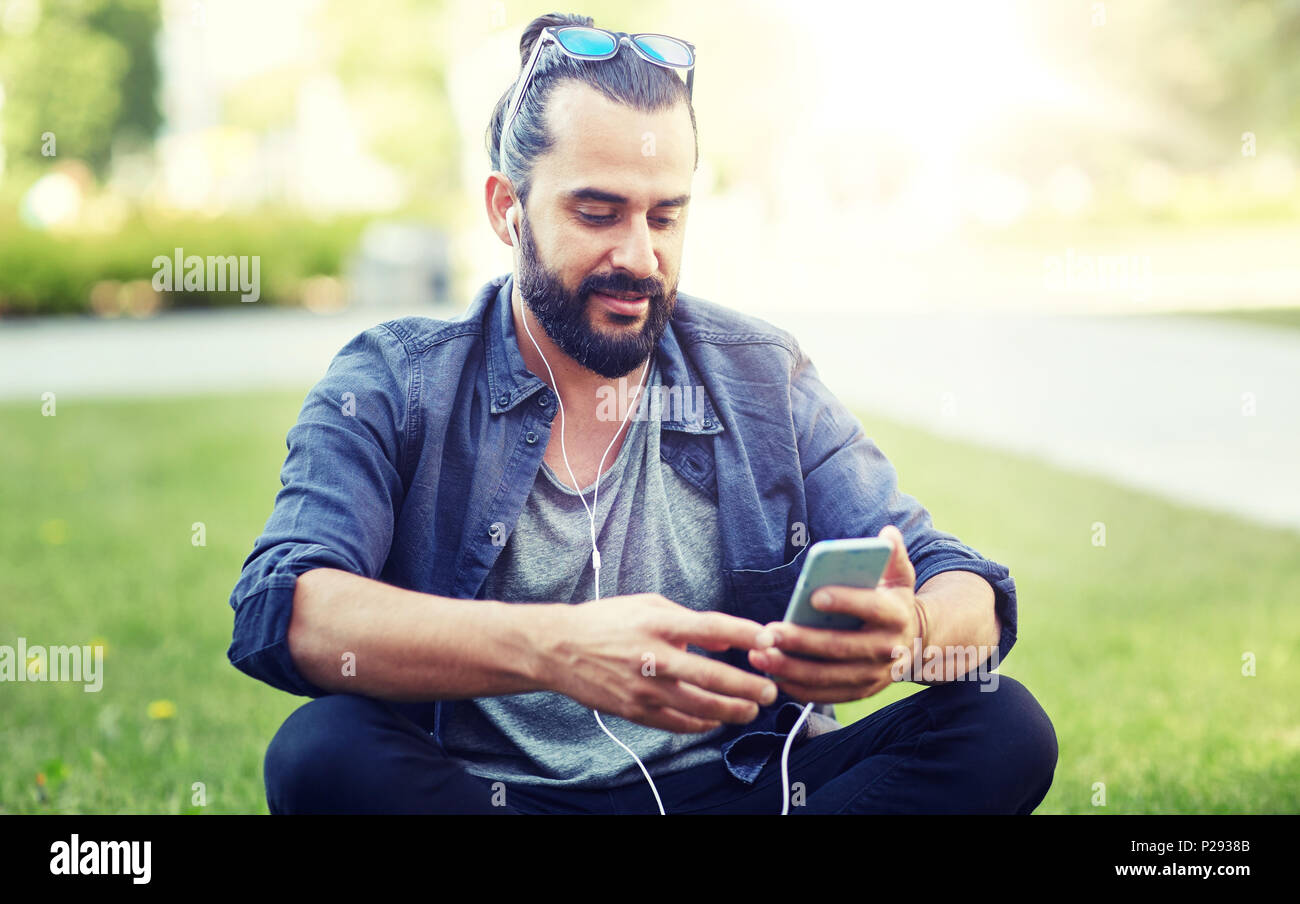 Mann mit Kopfhörern und Smartphone sitzen auf Rasen Stockfoto