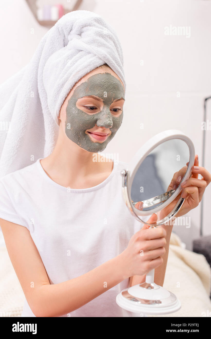 Junge Frau mit kosmetischen Clay Mask am Spiegel zu Hause suchen Stockfoto