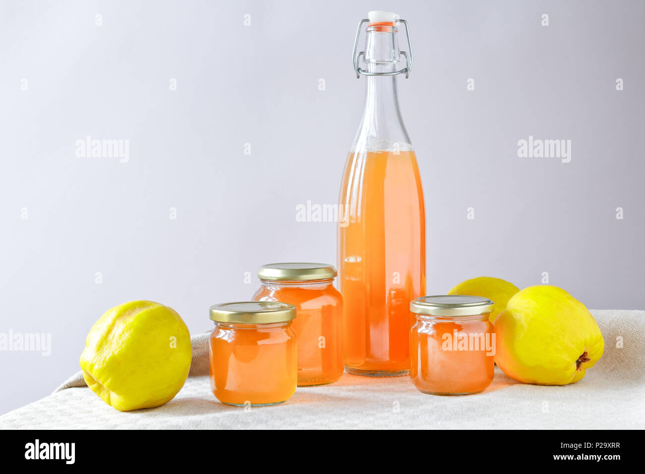 Hausgemachte Quitten Gelee und Saft in Flaschen und Gläsern mit Quitten auf Leinen Tischdecke vor neutralem Hintergrund, kopieren. Stockfoto