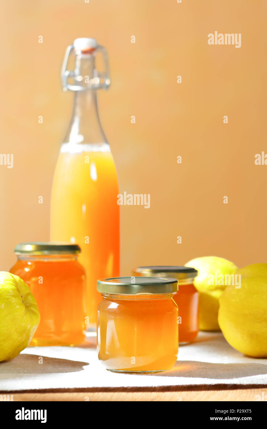 Hausgemachte Quitten Gelee und Saft in Flaschen und Gläsern mit Quitten auf Leinen Tischdecke im hellen Sonnenschein vor einem gelben und orangefarbenen Hintergrund Stockfoto