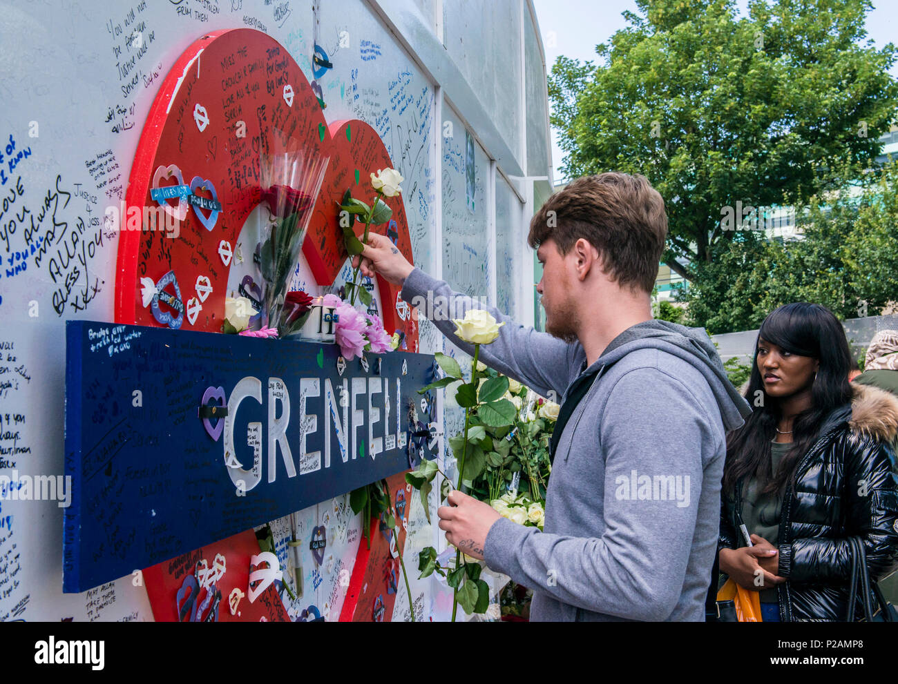 Junges Paar sie Blumen auf der Basis von Grenfell Tower, dem Jahrestag des Brandes, London, England, Großbritannien, 14. Juni 2018 Stockfoto
