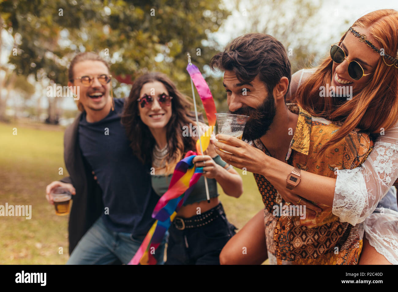 Gruppe junger Leute genießen Sie einen Tag in Music Festival. Paar huckepack und trinken Bier mit Freunden im Park. Stockfoto