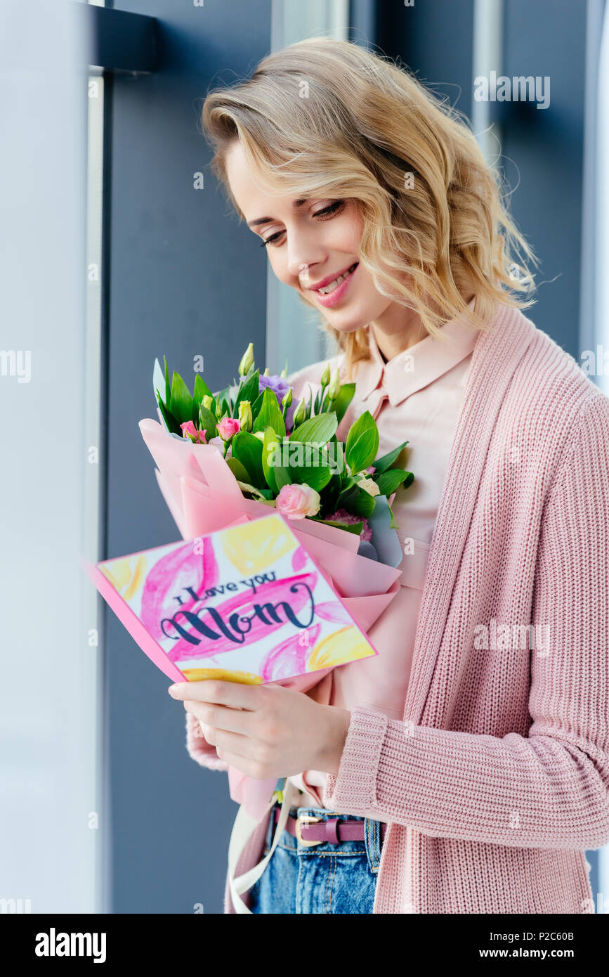 Lächelnde Frau mit Blumenstrauß lesen Ich liebe dich Mama Postkarte, Muttertag Konzept Stockfoto