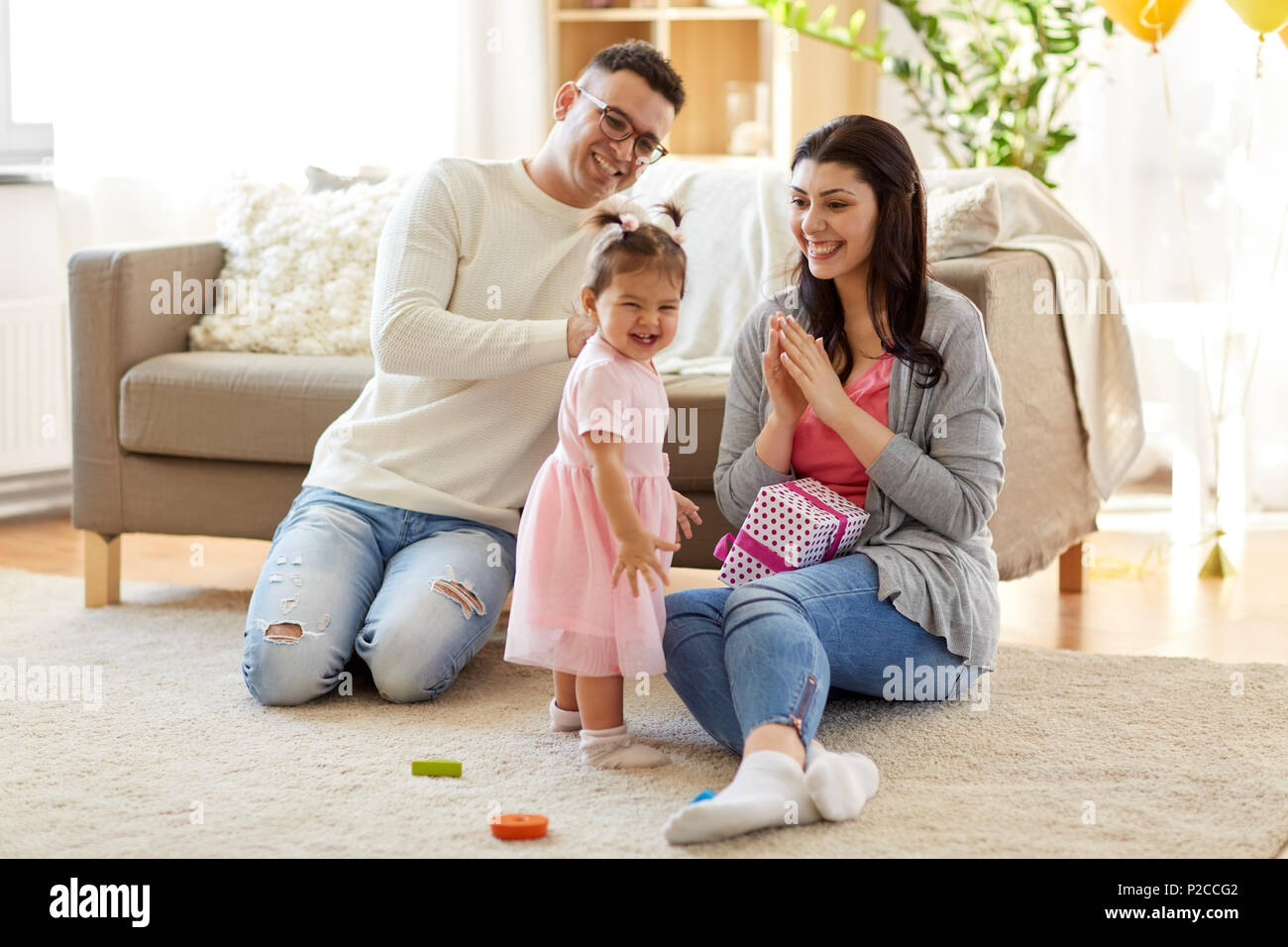 Baby Mädchen mit Geburtstagsgeschenk und Eltern zu Hause Stockfoto