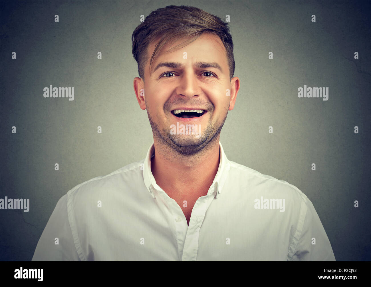 Portrait von gutaussehenden jungen Mann im weißen T-Shirt positiv an Kamera lachend auf grauem Hintergrund Stockfoto