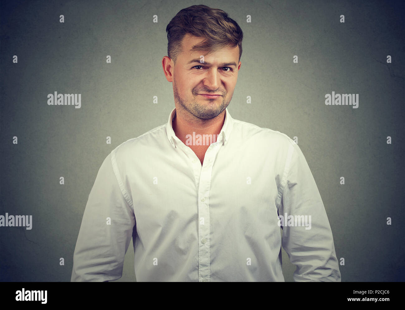 Junger Mann im weißen Hemd mit gerunzelter Stirn an Kamera schaut voller Skepsis und Misstrauen auf grauem Hintergrund Stockfoto