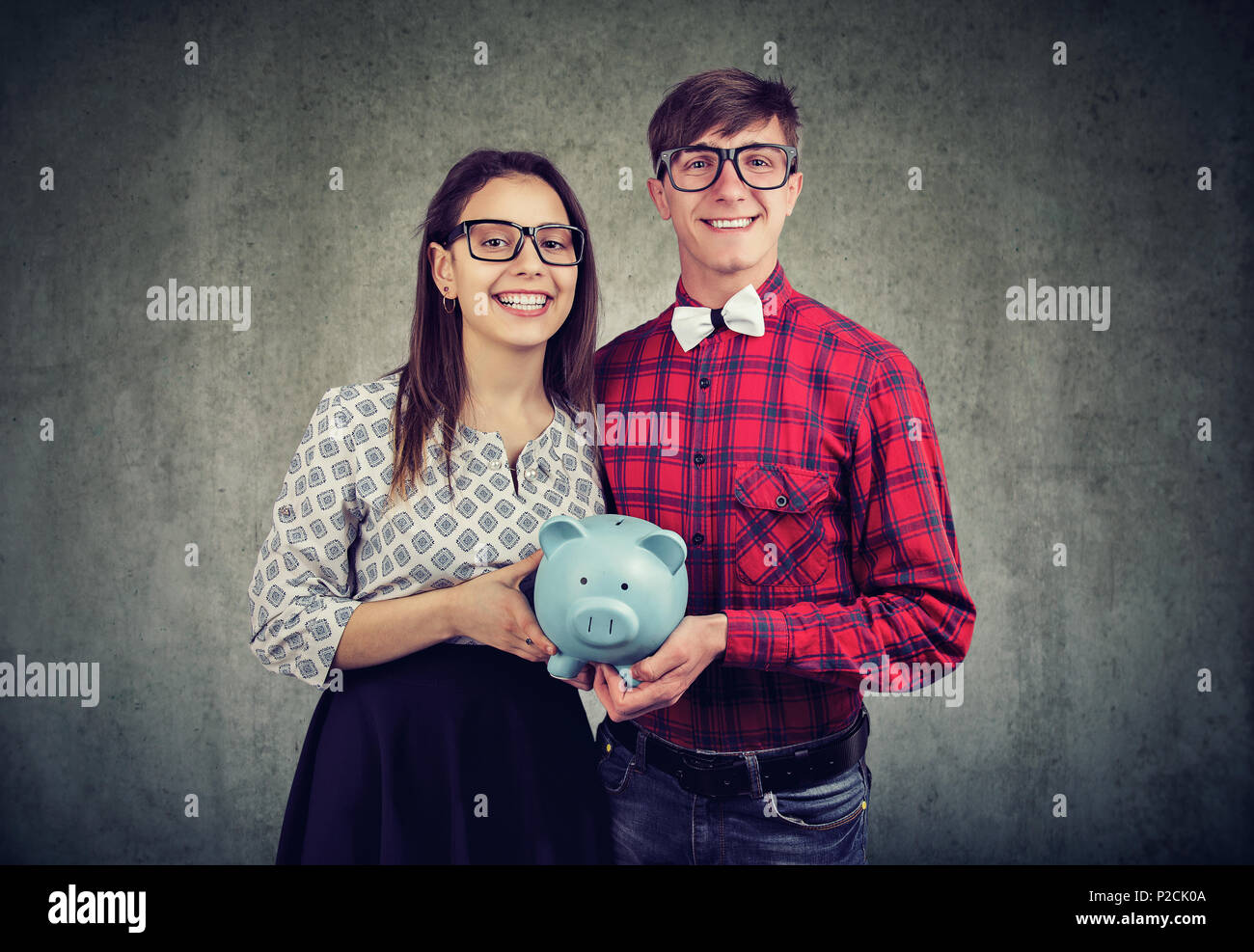 Fröhlicher Mann und Frau in Brillen holding money Bank zusammen mit gemeinsamen Haushalt lächelnd an Kamera zufrieden. Stockfoto