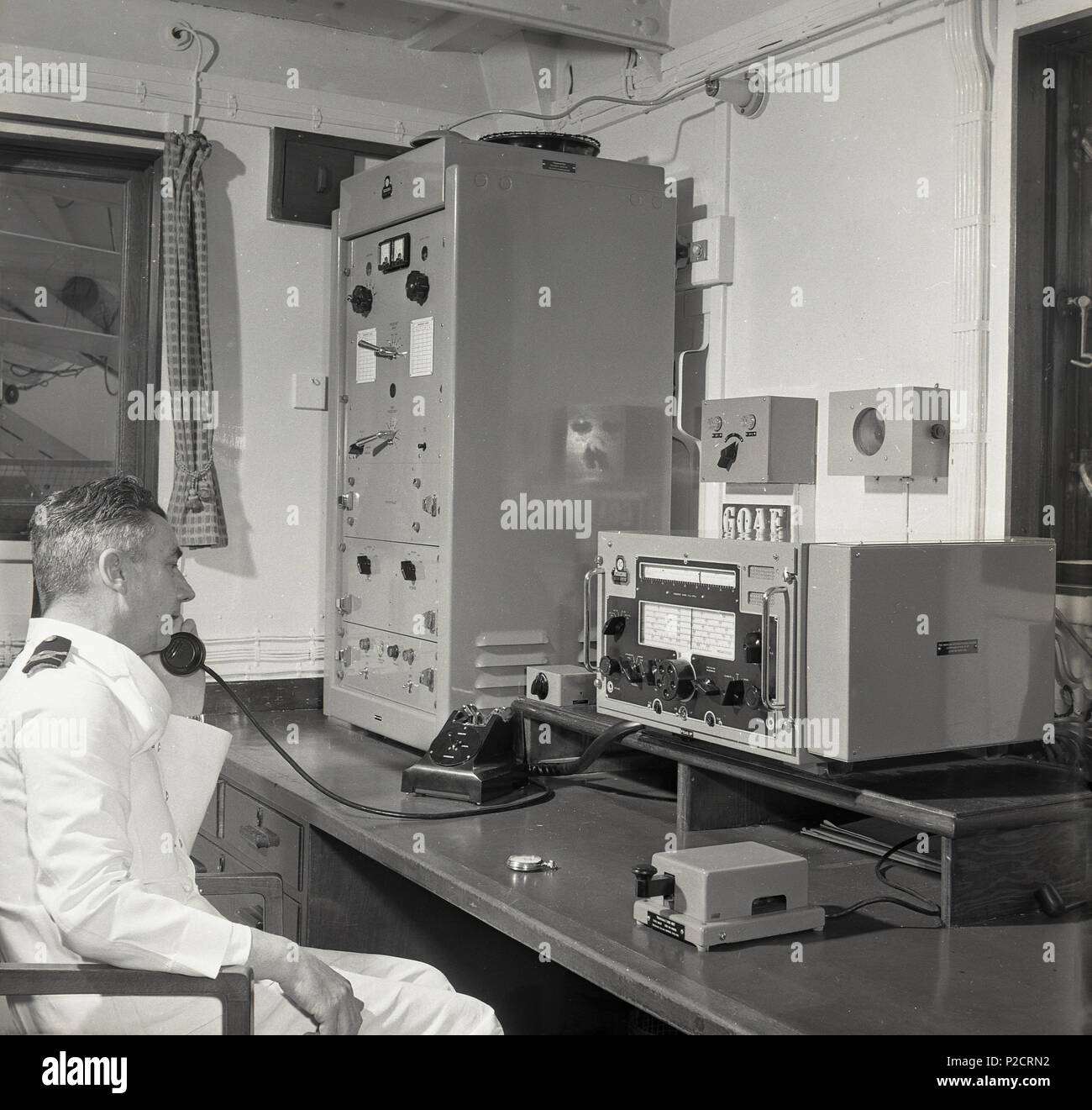 1950, historische, auf einem Passagierschiff im Radio Zimmer, ein uniformierter Mann wireless oder Funker an seinem Schreibtisch im Telefon können Sie über die Kommunikationseinrichtungen der Ära. Die primäre Rolle der Operator's war "Sicherheit auf See". Stockfoto