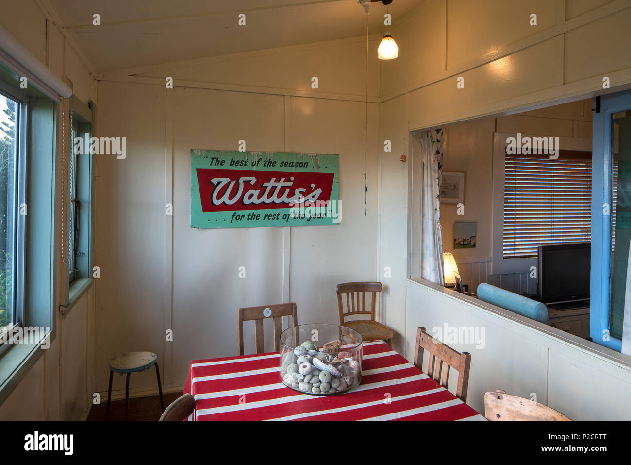 Essbereich des alten Bach/Strand Haus mit rot-weiß gestreiften Tisch und alte Stühle und alte Werbung watties Zeichen an der Wand. Historische Pourerere Stockfoto