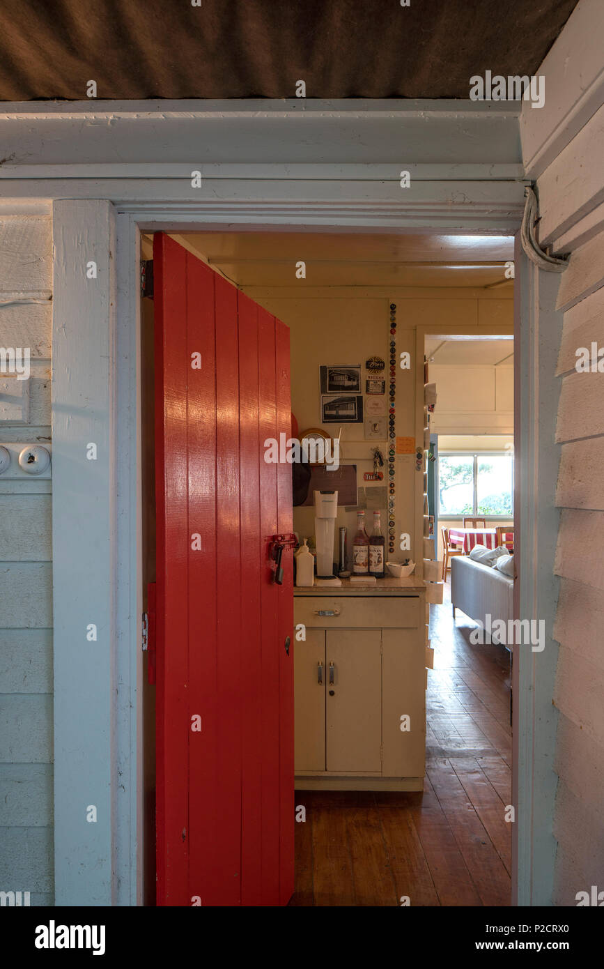 Durch die Hintertür auf die Innenseite des alten Bach/Beach House erschossen. rote Tür. Historische Pourerere Bach/Beach House, Hawke's Bay, Neuseeland mit neuen Linux-migration Stockfoto