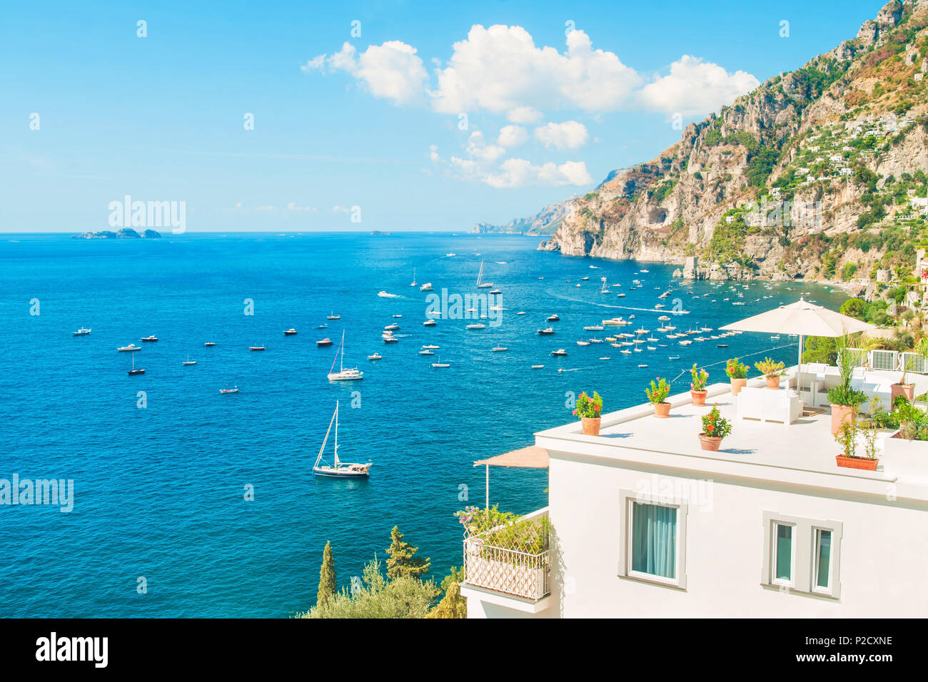 Weiße Ferienhaus mit Balkon und Dachterrasse mit Blick auf das Mittelmeer mit Bergen im Hintergrund an sonnigen Sommertagen, Positano, Amalfi Küste Stockfoto