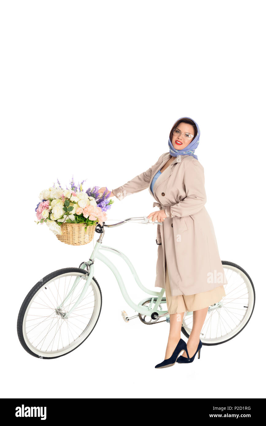 Schöne Übergrößen Frau in stilvollen Trenchcoat und Halstuch mit Vintage Fahrrad mit Blumen im Korb auf weißen isoliert Stockfoto